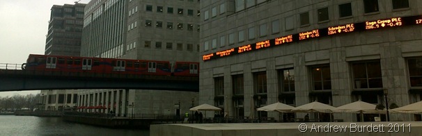 CANARY WHARF_The DLR runs through Canary Wharf. The orange text on the building's wall shows company stocks.