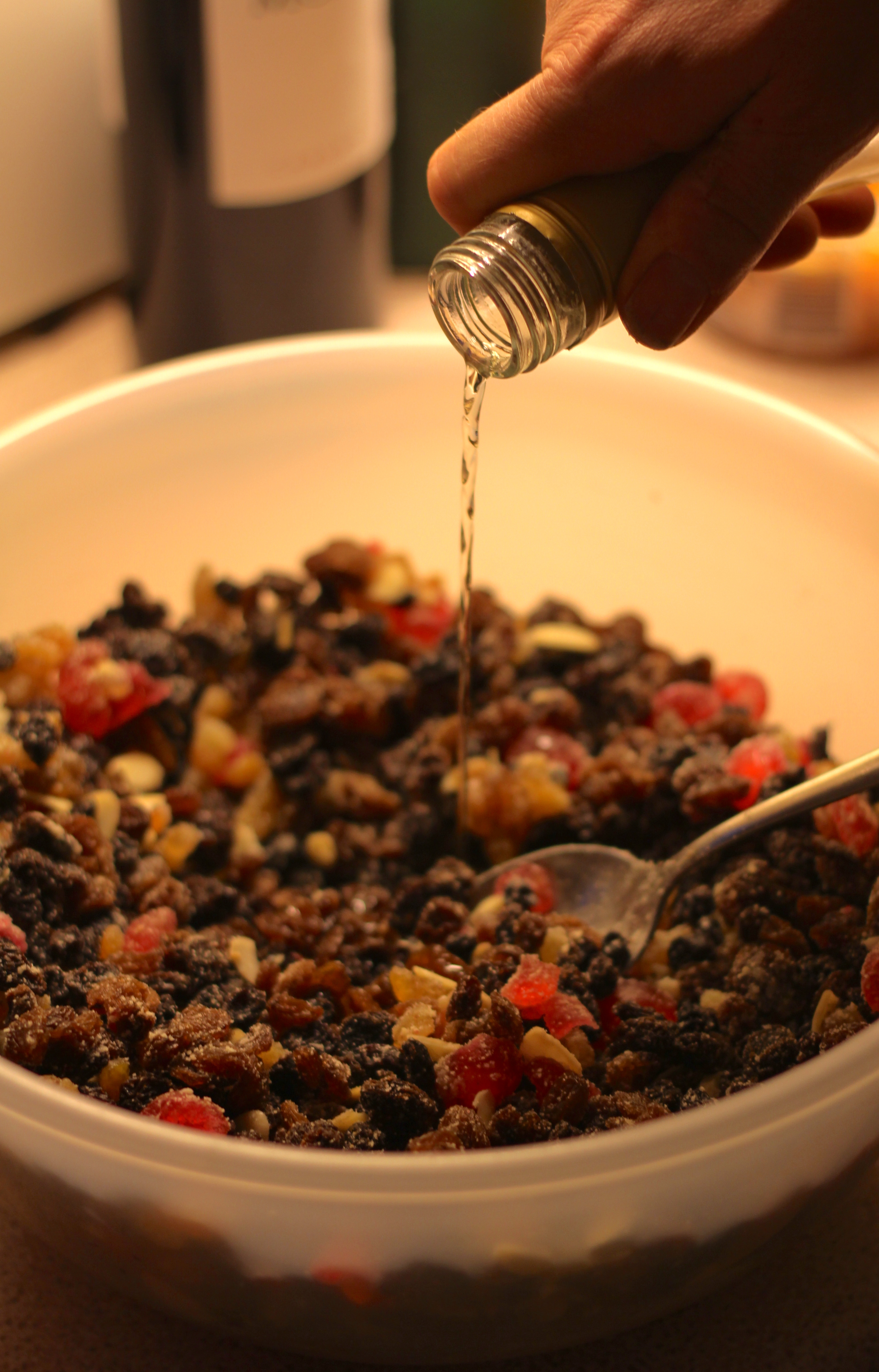 A bottle of brandy is poured into a mixture-bowl filled with fruit.