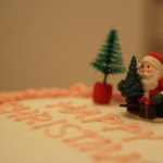 A Father Christmas character sitting beside a Christmas tree, atop our cake.