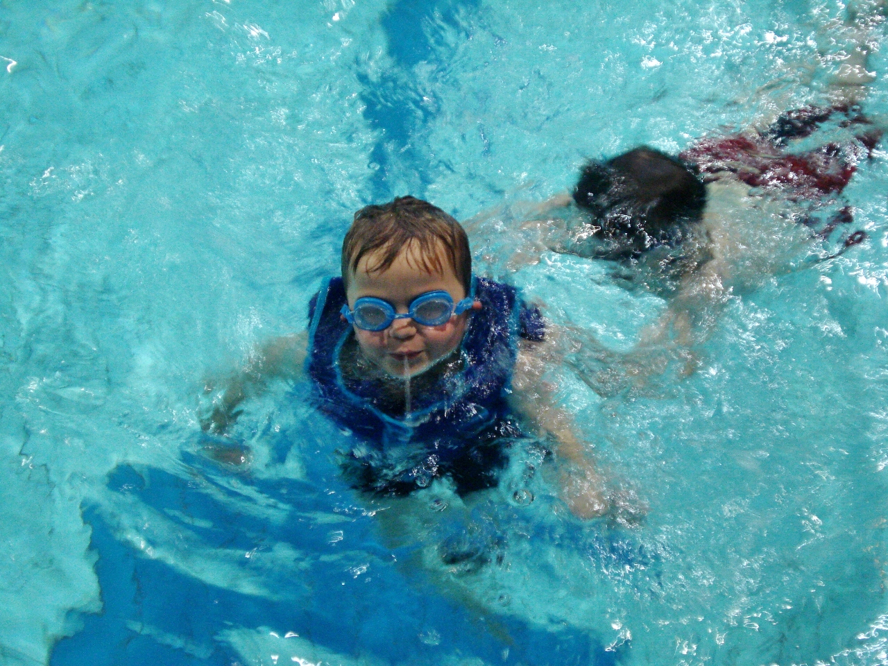 A child wearing a buoyancy-aid swims with his older brother.
