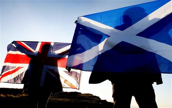 Sunlight forms silhouettes of campaigners on the flags of the United Kingdom and Scotland.