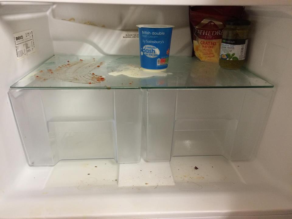 A messy fridge with spilt yoghurt on one shelf.